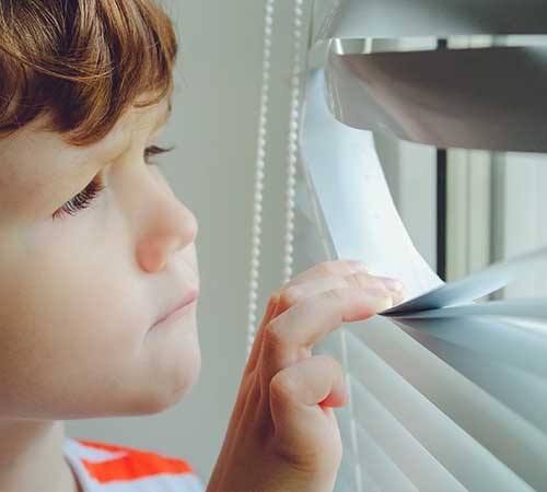 child looking out of window blinds with hands on louvres